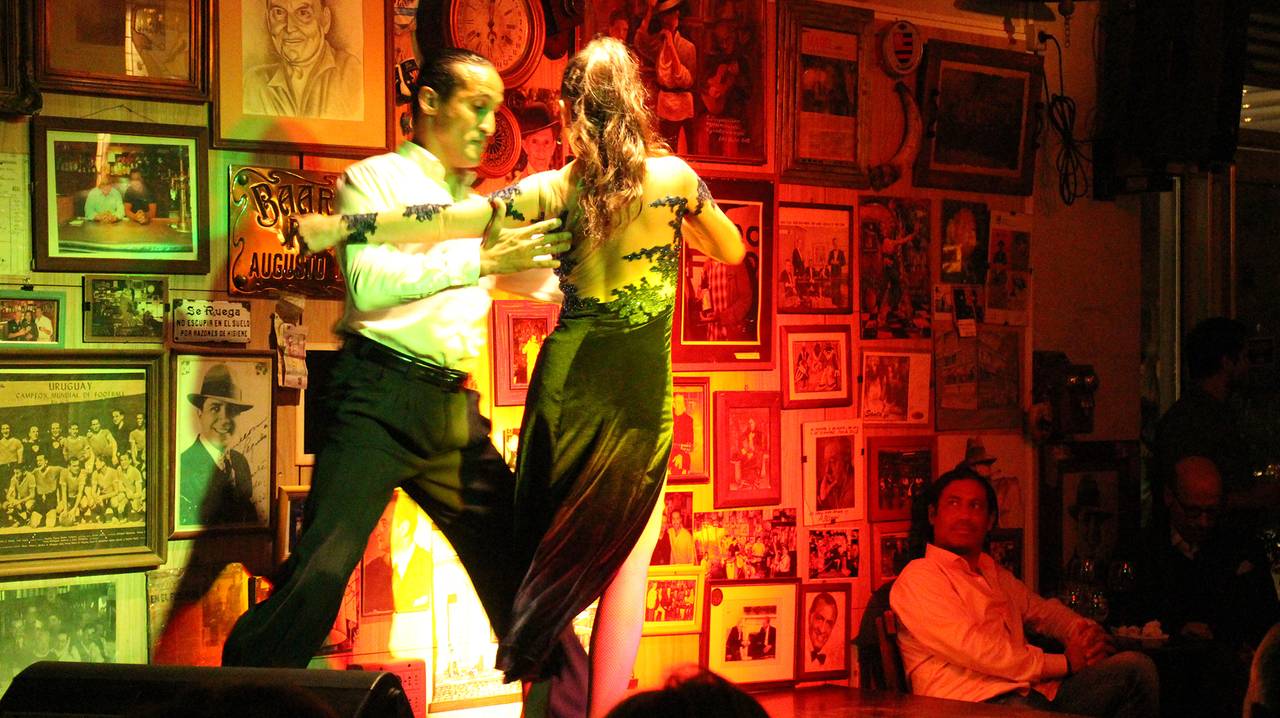 Pareja bailando tango frente a la pared de cuadros de Bar Fun Fun
